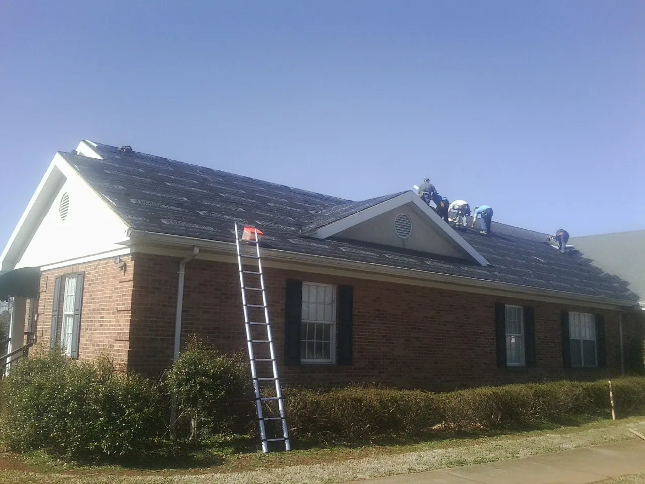 Crew tearing shingles off a brick ranch roof with a ladder set — Metal Roof Repair work by our crew in Lavalette