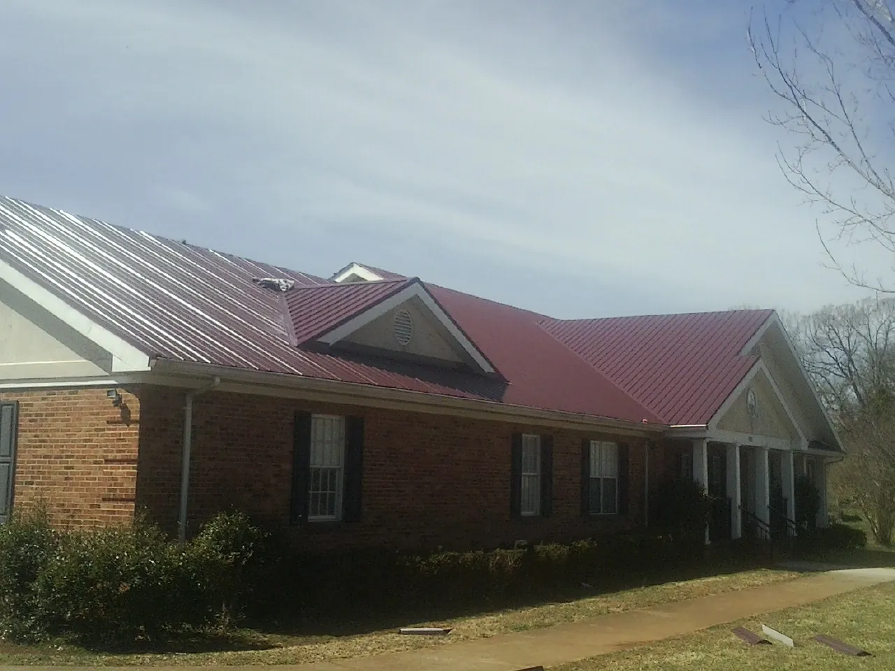 Red metal roof with gabled entries on a long brick building, from a Hail Damage Roof Repair job in Lavalette