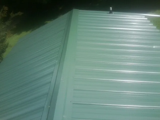 New green metal panels meeting at the ridge of a roof — Flat Roof Repair work by our crew in Lavalette