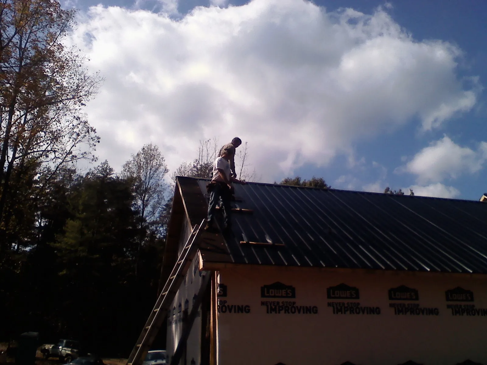 Roofer fastening dark metal panels high against a cloudy sky, from a Roof Inspection job in Lavalette