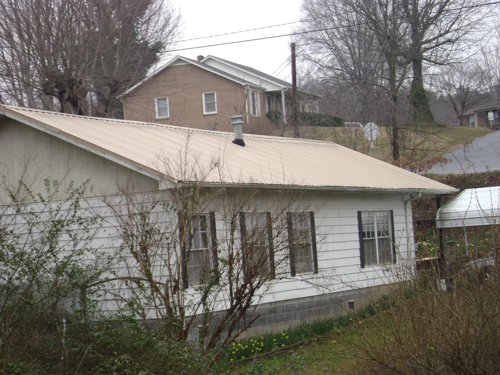 Tan metal roof on a white sided house set into a hillside — Commercial Roofing by Roofing Brothers in Lavalette