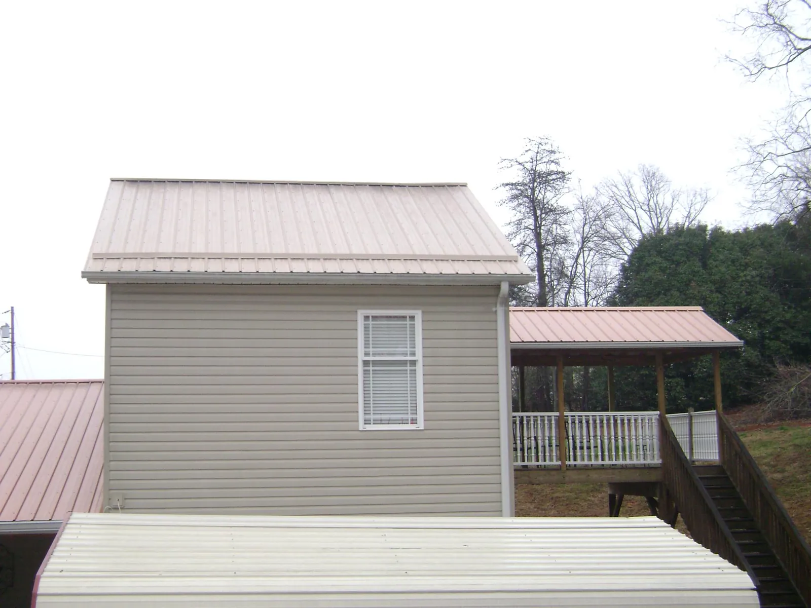 Tan metal roofs on a two story addition and attached porch, from a Roof Replacement job in Lavalette